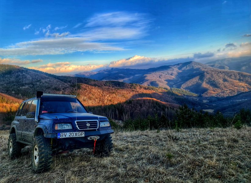 Off-road SUV on a grassy mountain landscape under a vibrant blue sky with clouds.