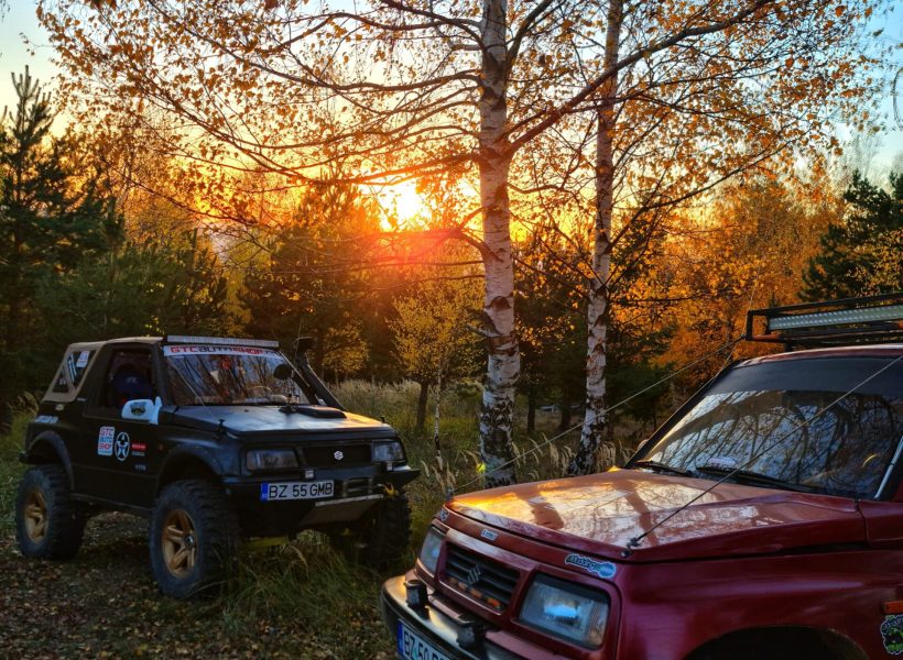 Two off-road vehicles parked among autumn trees at sunset.