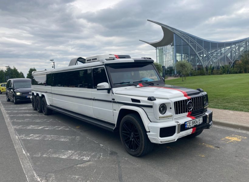 White luxury extended SUV limo parked outside modern glass building.